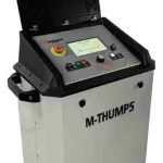 M-THUMP5 industrial machine with open lid, front control panel showing emergency stop, display, and buttons; grey enclosure with black top and handles.