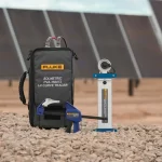Fluke Solmetric I-V curve tracer and accessories set on rocky ground with solar panels in the background.